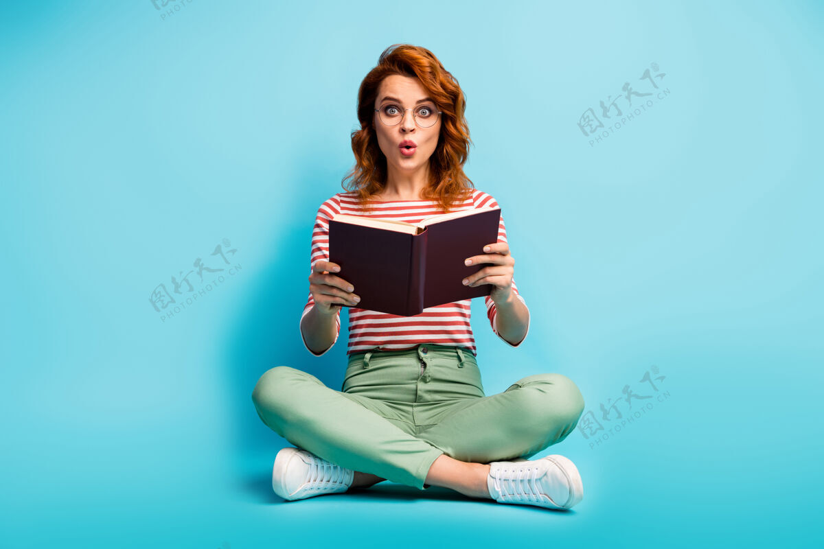 地板全尺寸照片惊讶的女人坐着双腿交叉阅读书籍难以置信的小说故事印象深刻的尖叫哇omg穿绿白色衣服隔离蓝色学习惊喜情绪