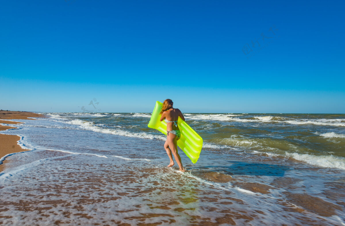 美丽穿着泳装的漂亮苗条的年轻女子拿着气垫在沙滩上奔跑女性泡沫热带