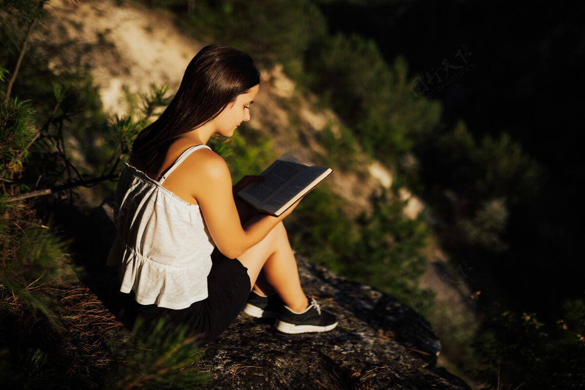 生活方式年轻的女孩在看书 而坐在美丽的自然风景享受天农作物