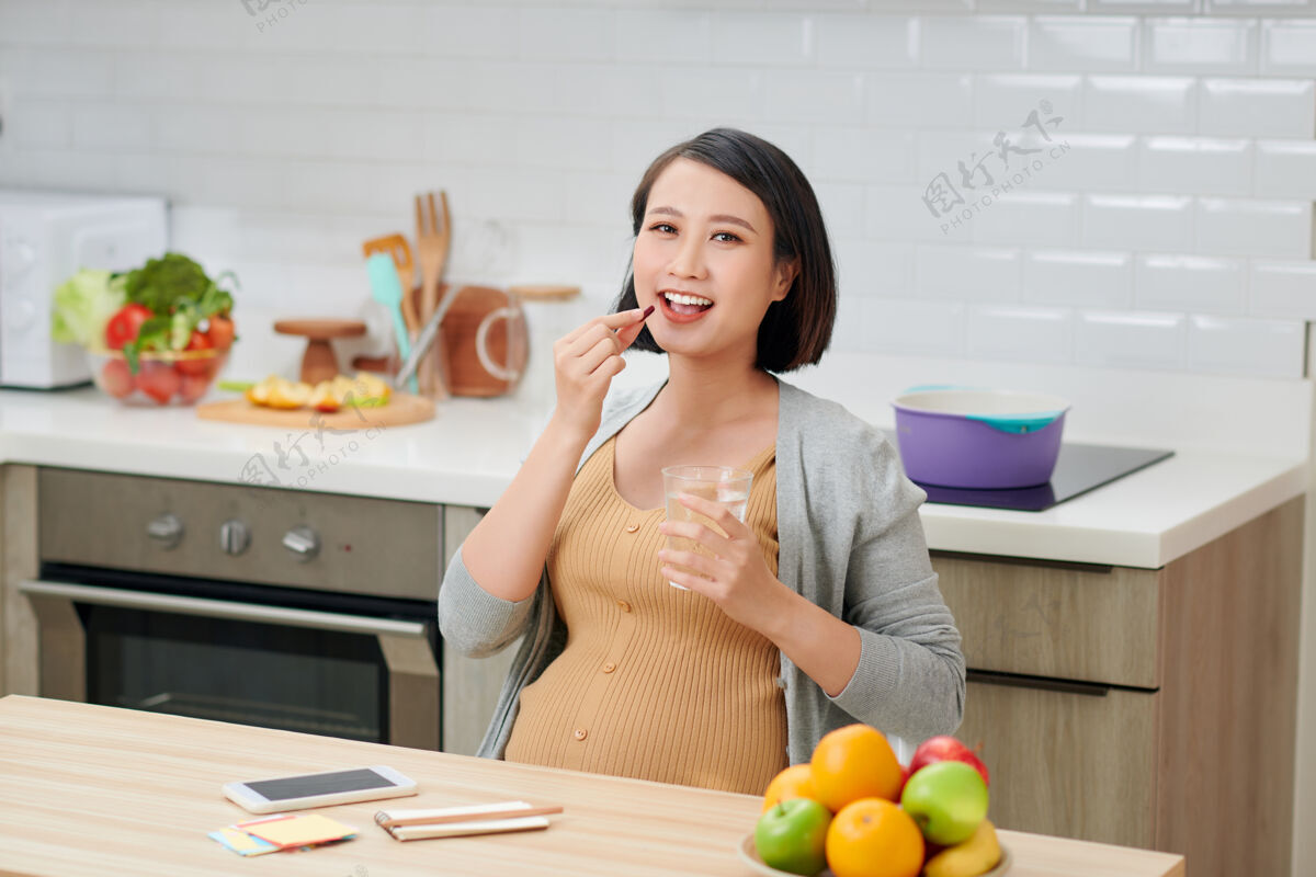 期望孕妇拿着维生素药片和一杯水放在厨房里孕妇女孩成人