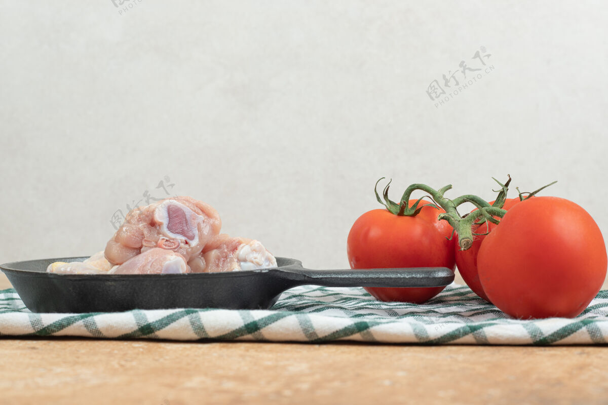 肉一个深色的平底锅 里面有生鸡腿和西红柿生的未煮熟的大理石