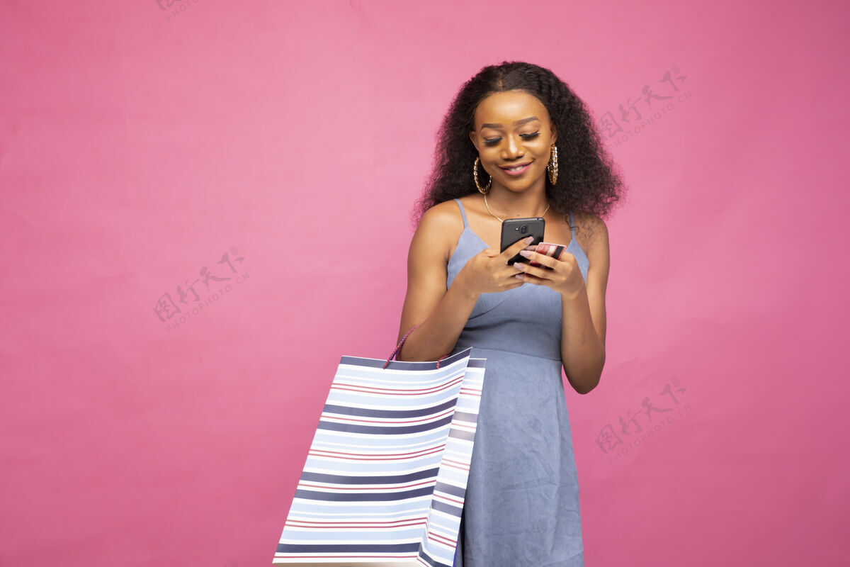 购物美丽的非洲女性在社交媒体上用她的智能手机发布她的购物狂潮持有非洲包