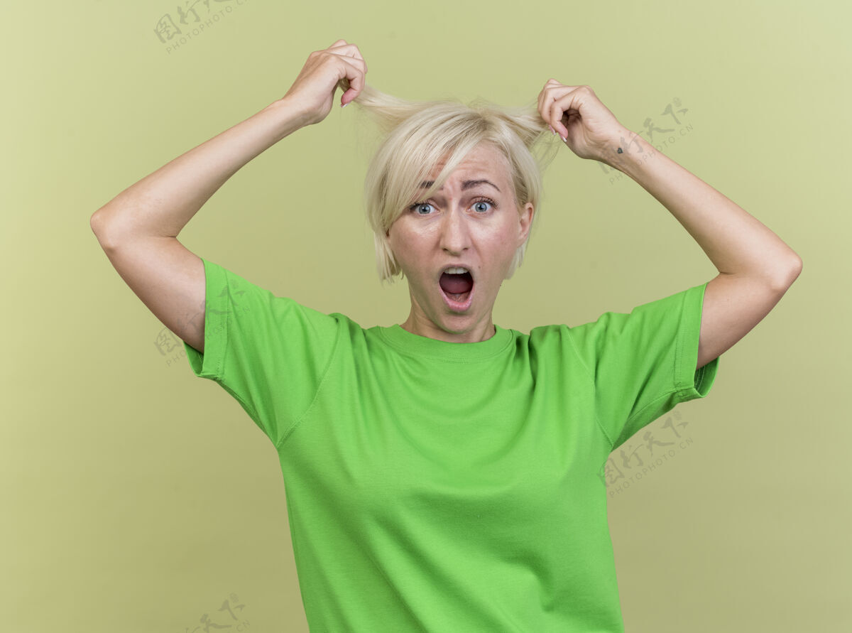 压力紧张的中年金发斯拉夫妇女看着相机抓住头发孤立的橄榄绿背景斯拉夫人女人绿色