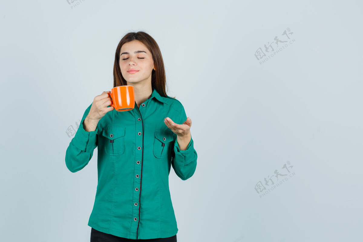 衬衫年轻女士端着一杯桔黄色的茶 展示着衬衫上的东西 看上去很平静前视图东西成人牙齿