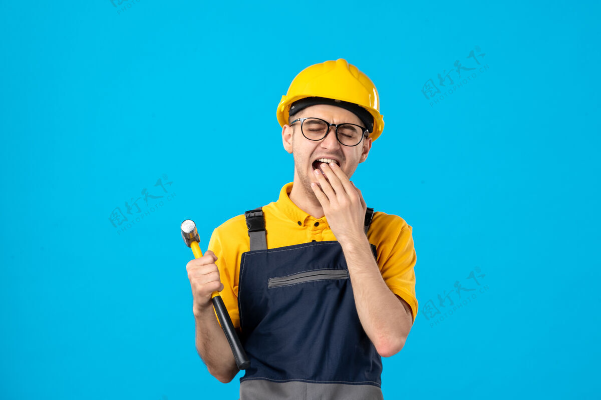 表面前视图打呵欠的男工人穿着黄色制服在蓝色建筑服务承包商