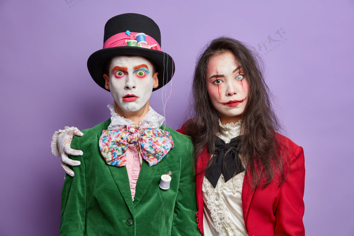 恐惧两个穿着万圣节狂欢节服装的朋友拥抱并拥有友好的关系 带着诡异的妆容在紫色的墙上庆祝节日死亡节日服装