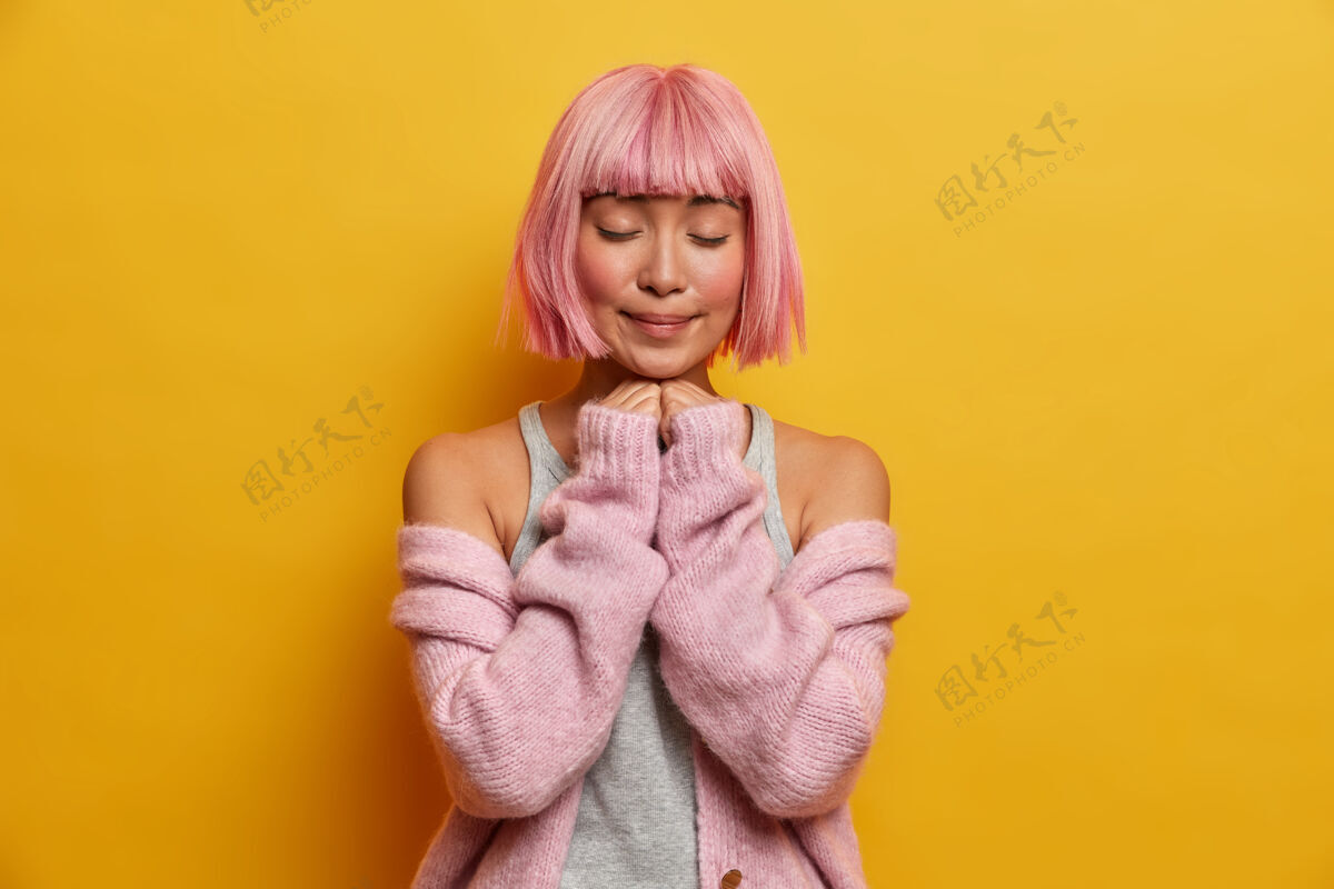 发型可爱的女人有着粉红色的bob发型和流苏 站在室内 闭上眼睛 手放在下巴下面时尚Bob女士