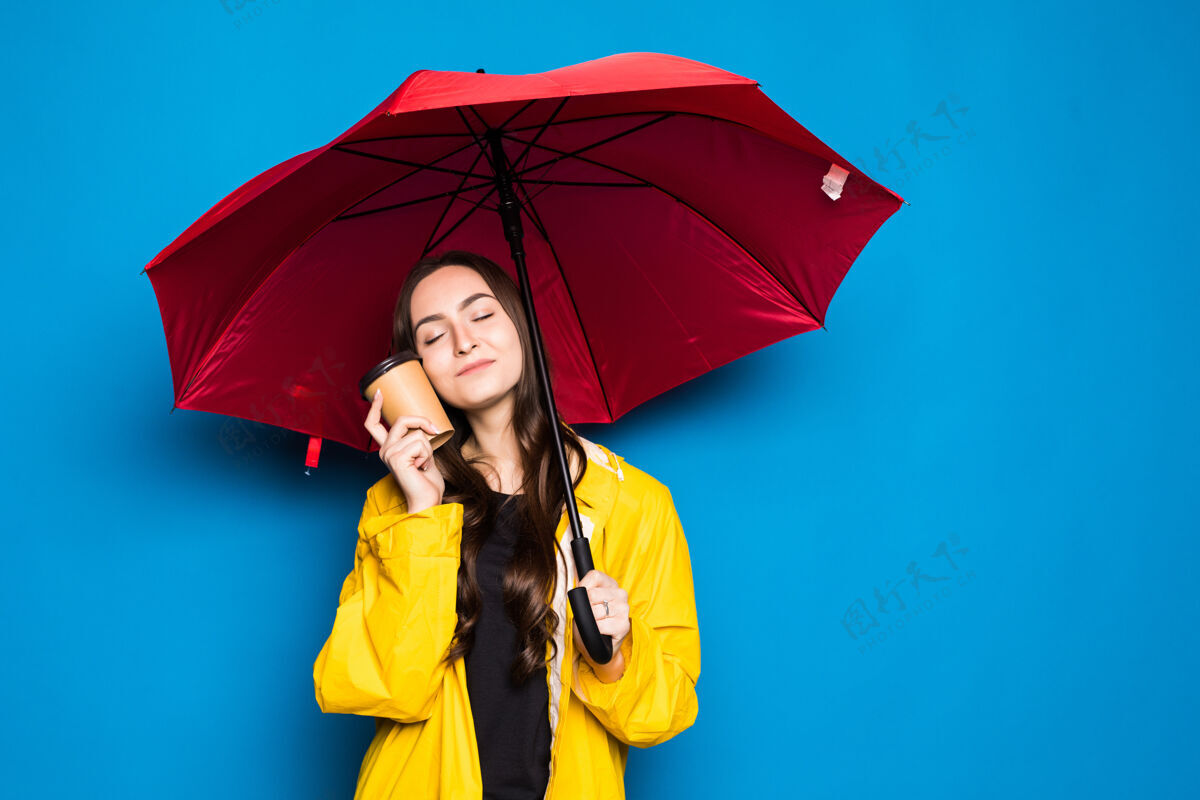 水坑穿着雨衣的中国年轻女子撑着雨伞 隔着孤零零的蓝色墙壁 非常高兴地用手和手指指着积极女人坏