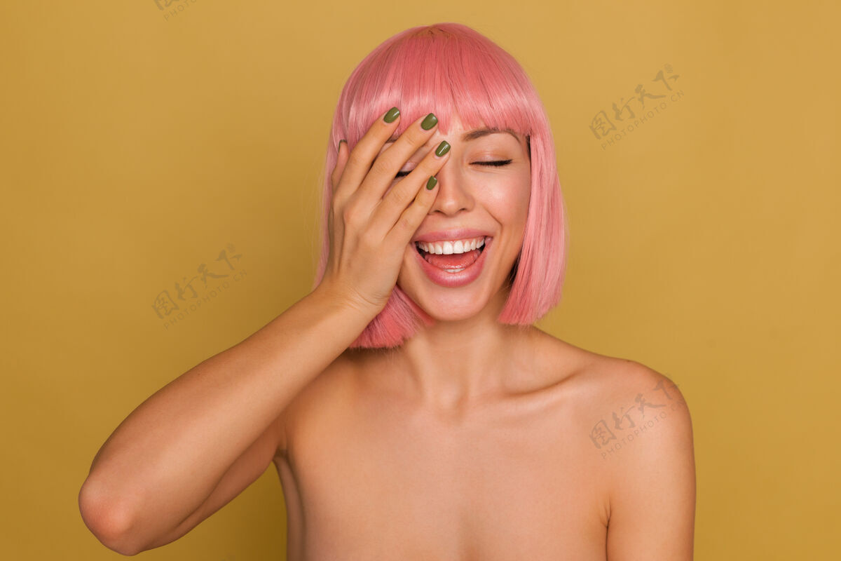 欧洲美丽快乐的年轻女士的肖像 粉色短发 手举 脸上涂着绿色指甲 闭着眼睛开心地笑着 隔着芥末墙头发特写漂亮
