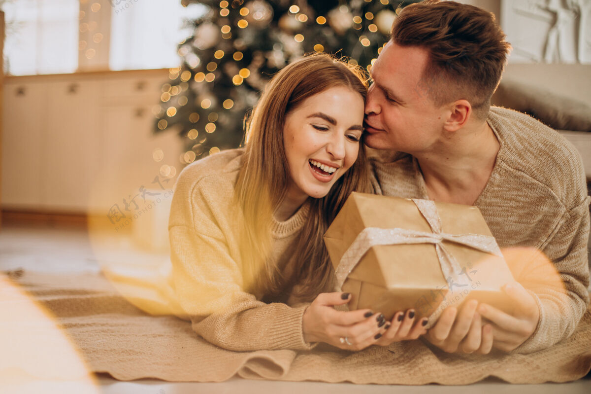 Bokeh一对年轻夫妇在圣诞树旁互相制作礼物家家庭圣诞灯