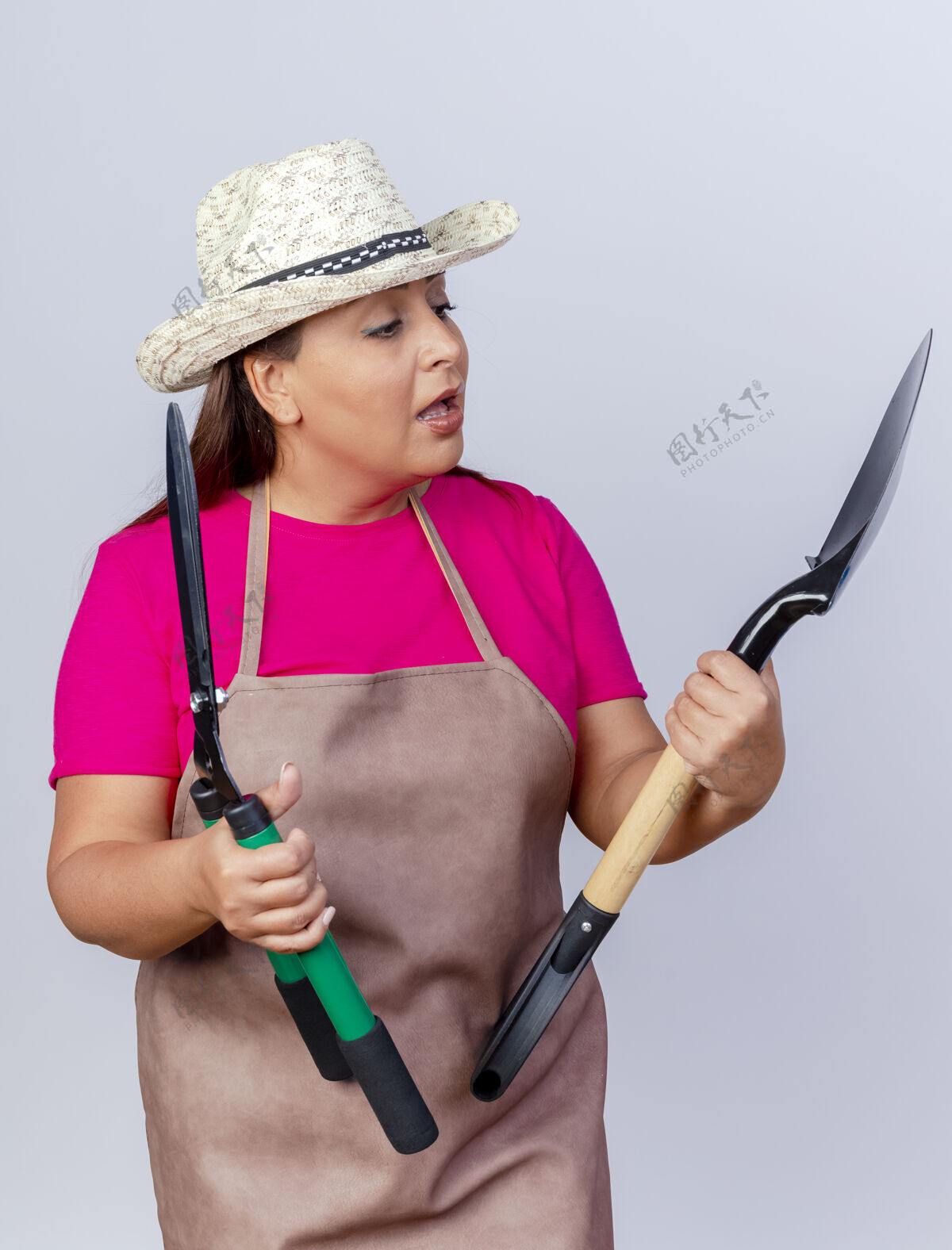举行穿着围裙 戴着帽子 拿着铲子和树篱修剪器的中年园丁们正困惑地看着他们站在白色的背景下做着选择剪子困惑花园