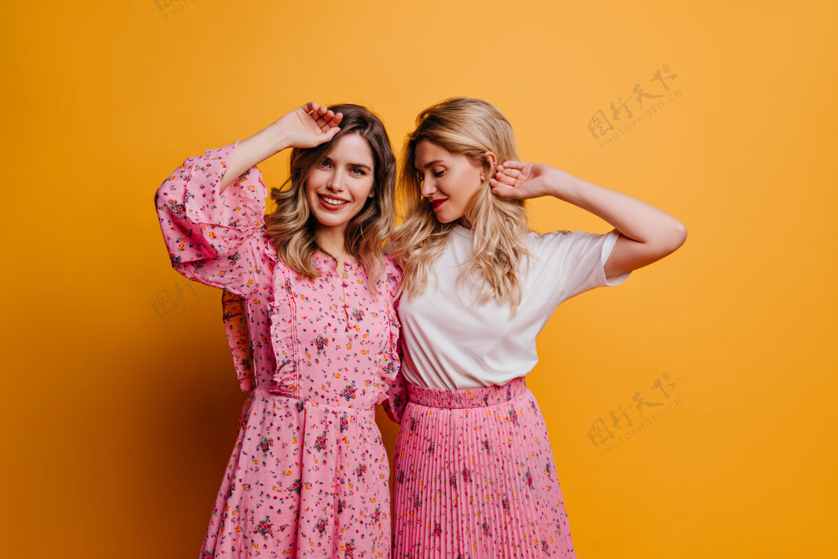 黑发迷人的女人穿着可爱的粉色连衣裙和妹妹一起度过休闲时光室内照片 令人惊叹的女模特表达积极的情绪快乐嬉戏快乐