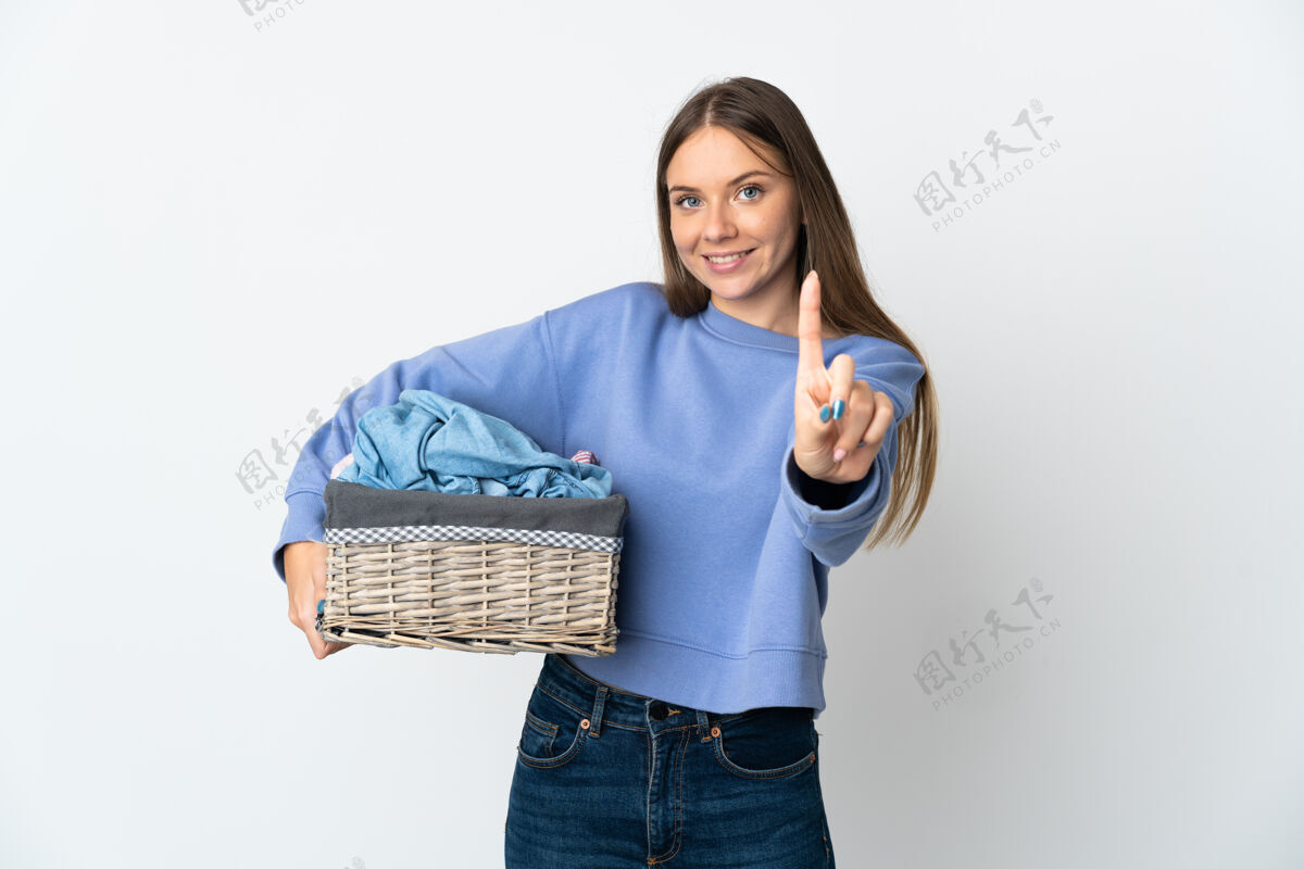 点年轻的立陶宛妇女拿着一个衣服篮子 在白色背景上孤立地展示和举起一个手指点人点