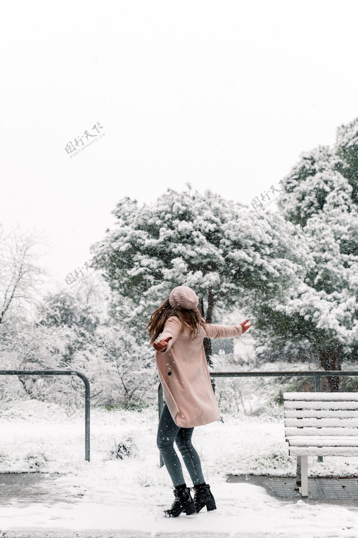 公园一个穿着暖和衣服的无忧无虑的女人 在公园里尽情享受冬天的雪天 张开双臂转过身来积极女人温暖的衣服