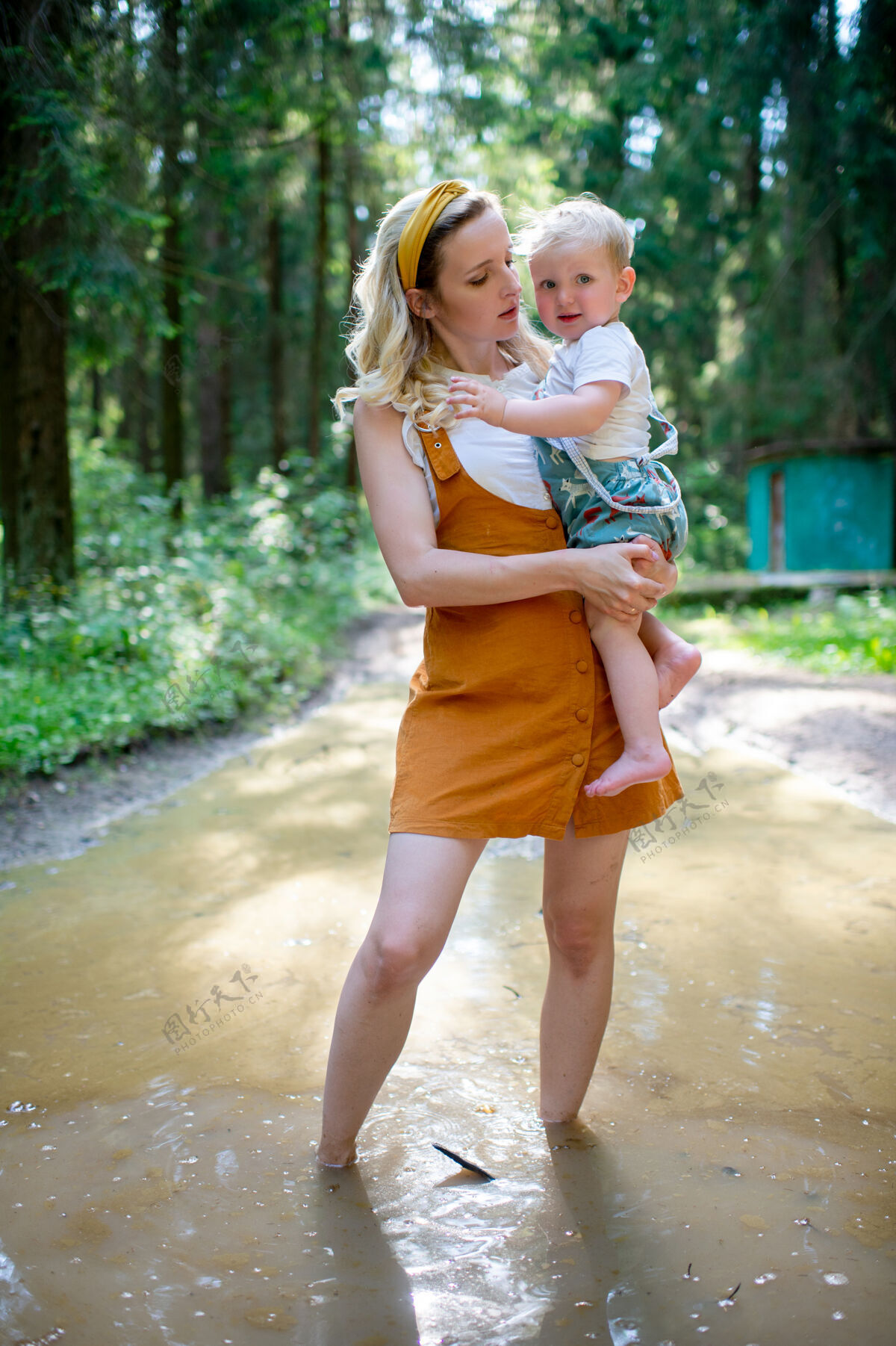 森林年轻的母亲抱着儿子站在森林的水坑里蹒跚学步搞笑家庭