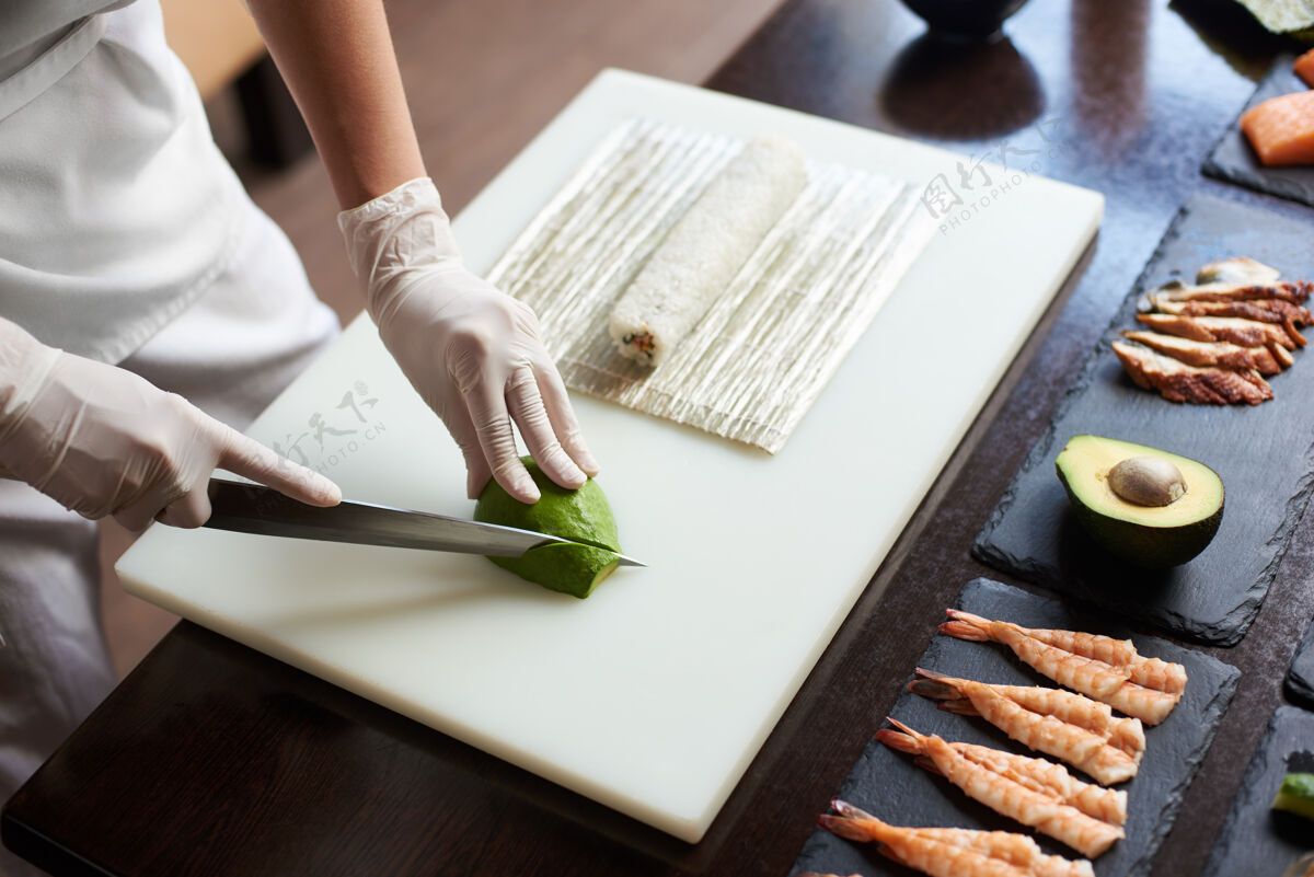 蔬菜在餐厅准备美味的卷寿司过程的特写镜头女手戴一次性手套在木板上用刀切鳄梨鱼美味烹饪