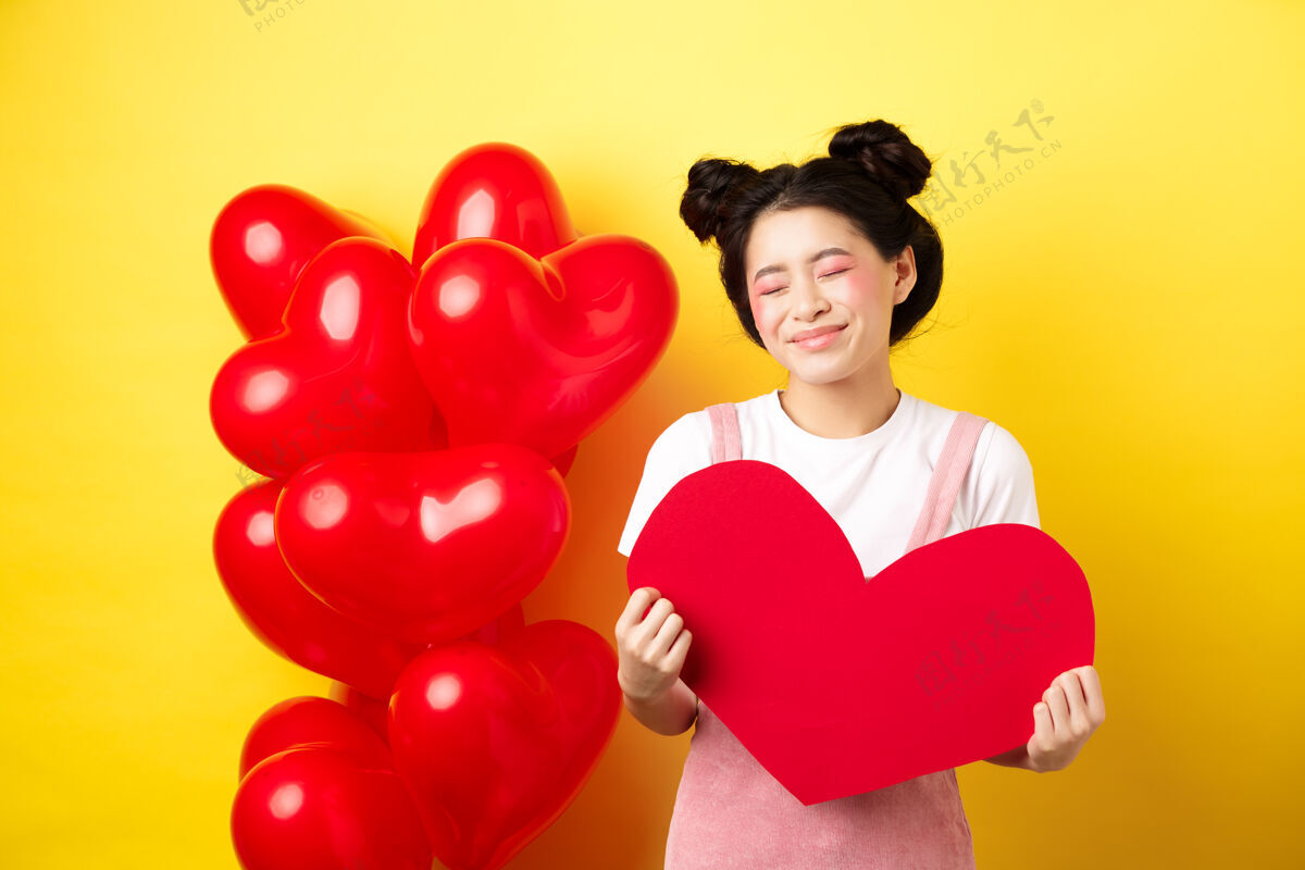 温柔情人节快乐愚蠢美丽的亚洲女人微笑着梦幻 展现着红心 想象着和情人的浪漫约会 站在黄色的背景上浪漫情感感情