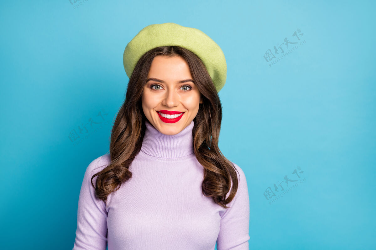 黑发照片惊人的旅行者女孩女士牙齿微笑微笑时尚的外观穿现代绿色贝雷帽紫色高领套头衫隔离明亮的蓝色墙壁女性服装时尚