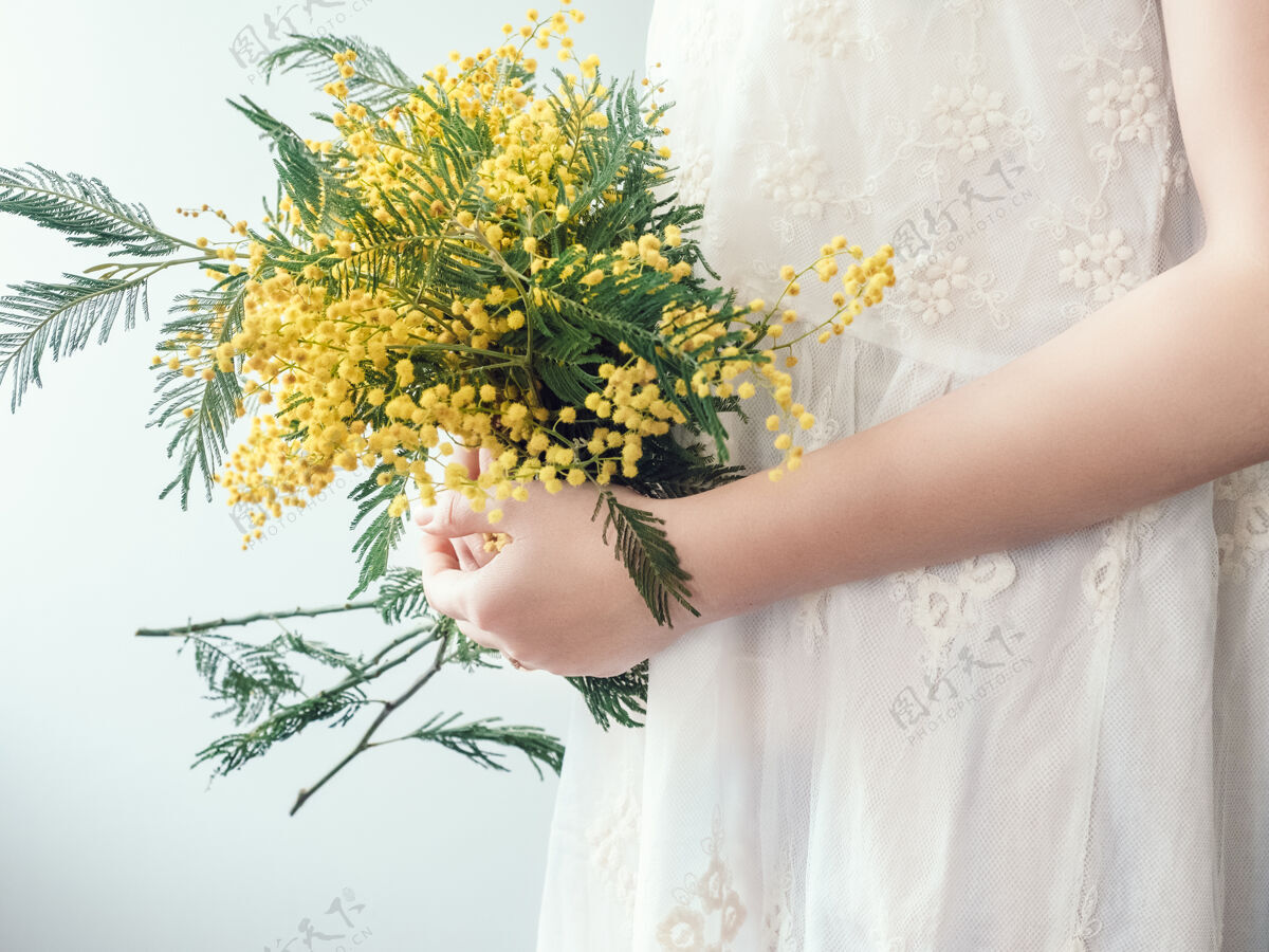开花一束明亮的黄色花朵在一个穿着白色连衣裙的年轻女子手里美丽浪漫白天