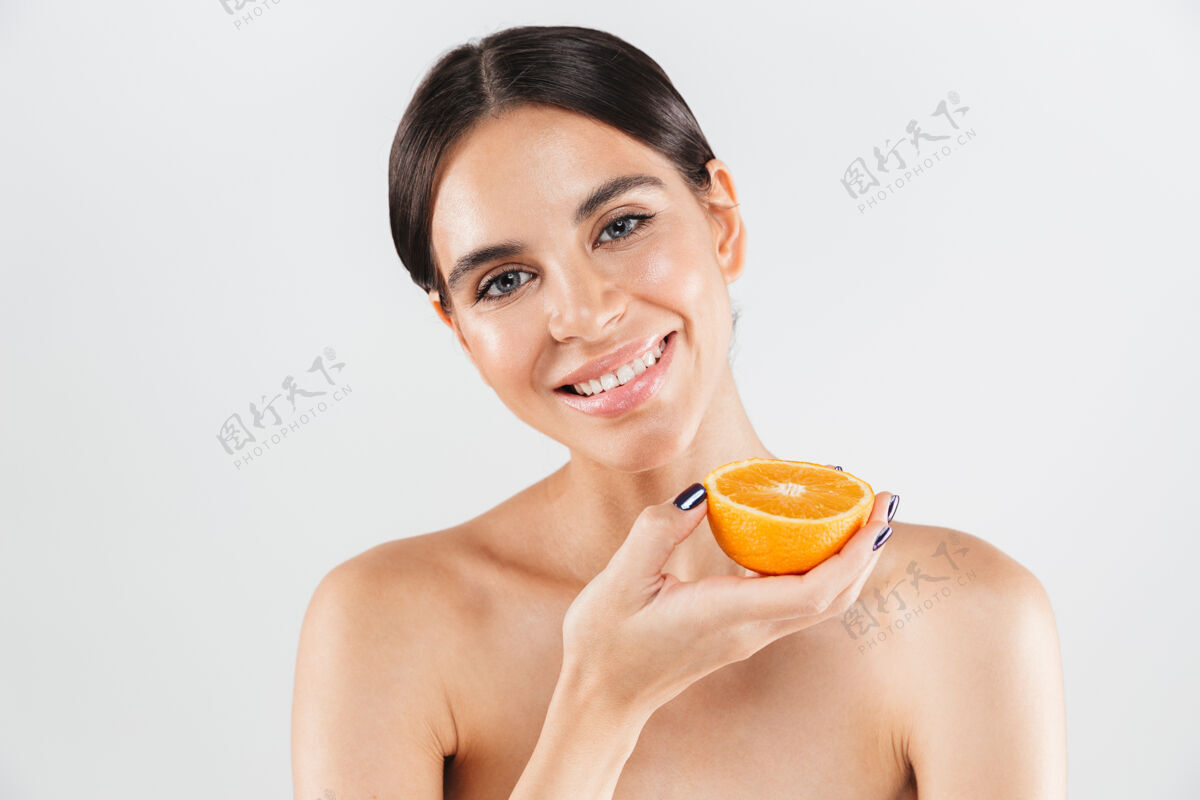 新鲜美丽的肖像画 一个迷人的健康的女人孤立地站在白色的墙上 摆着半个橘子的姿势黑发水疗身体