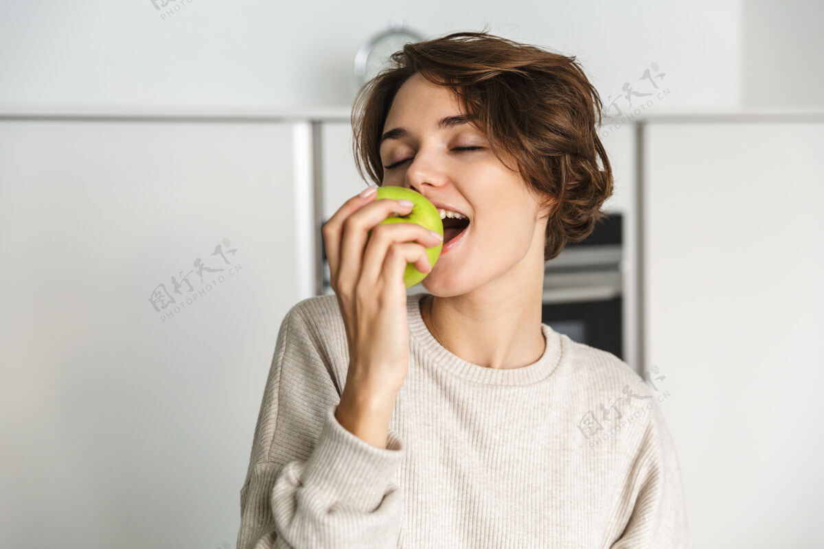 持有微笑的年轻女子在厨房里拿着青苹果品味肖像享受