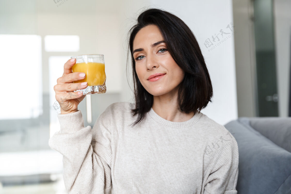 谎言一张30多岁的熟女在明亮的房间里坐在沙发上喝橙汁的照片玻璃吸引力成人