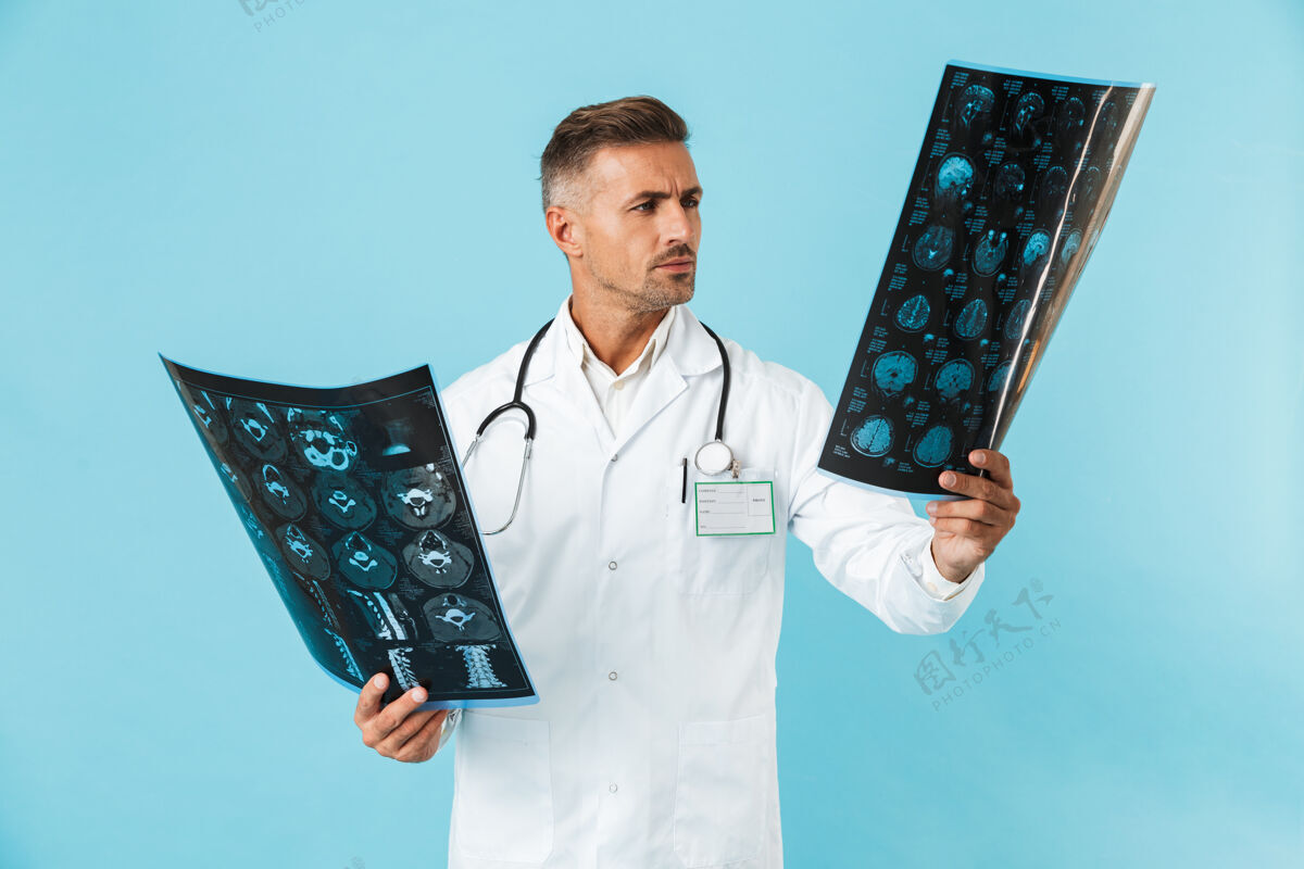 制服30多岁的医生手持听诊器 手持x光片 孤零零地站在蓝色的墙上医院职业X光