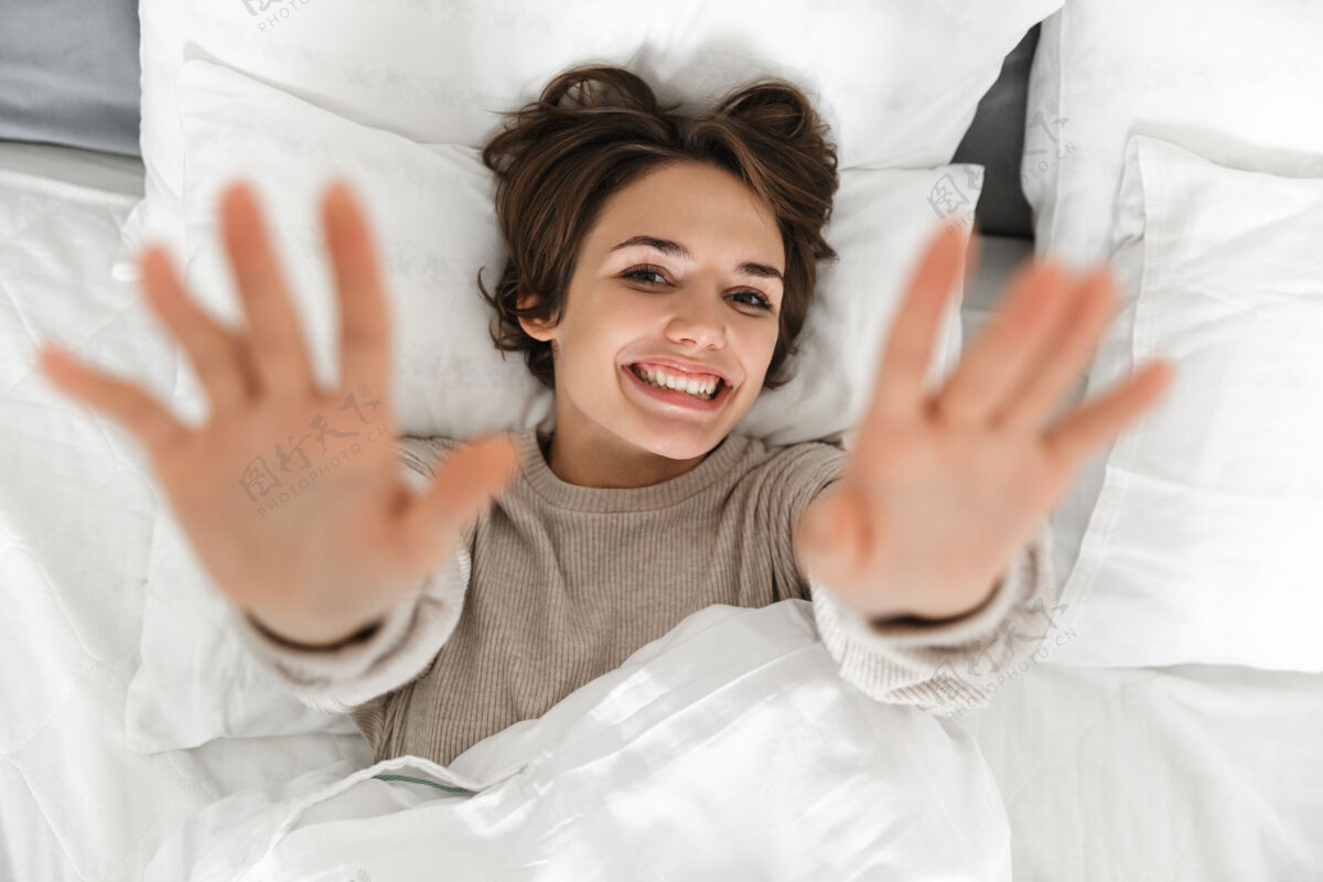 床单一个微笑的年轻女孩在床上放松的俯视图年轻枕头睡衣