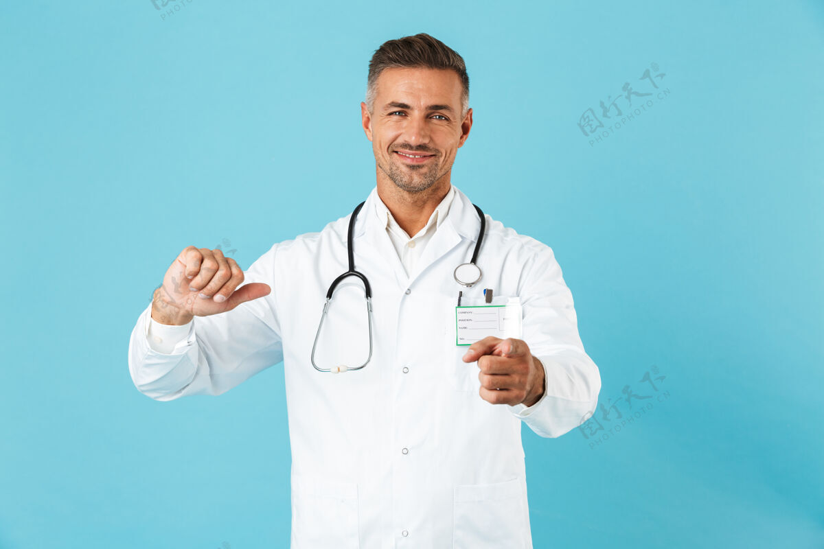 顾问自信的男人医生穿着制服孤立地站在蓝色的墙上 指着自己指点手势医院