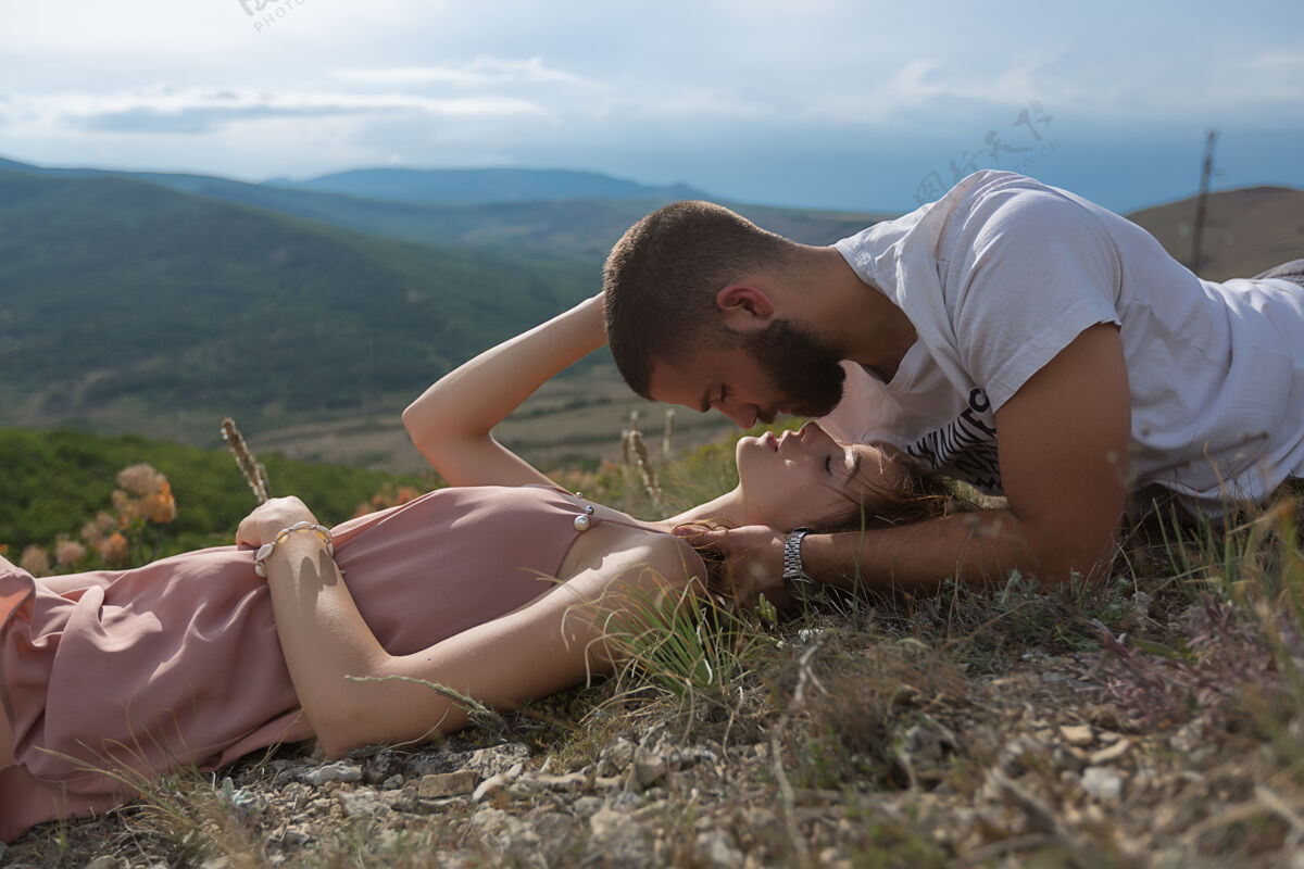 两个一对年轻的夫妇 一男一女 躺在草地上 在青山绿水的映衬下互相对视天空美丽自然户外假期风景