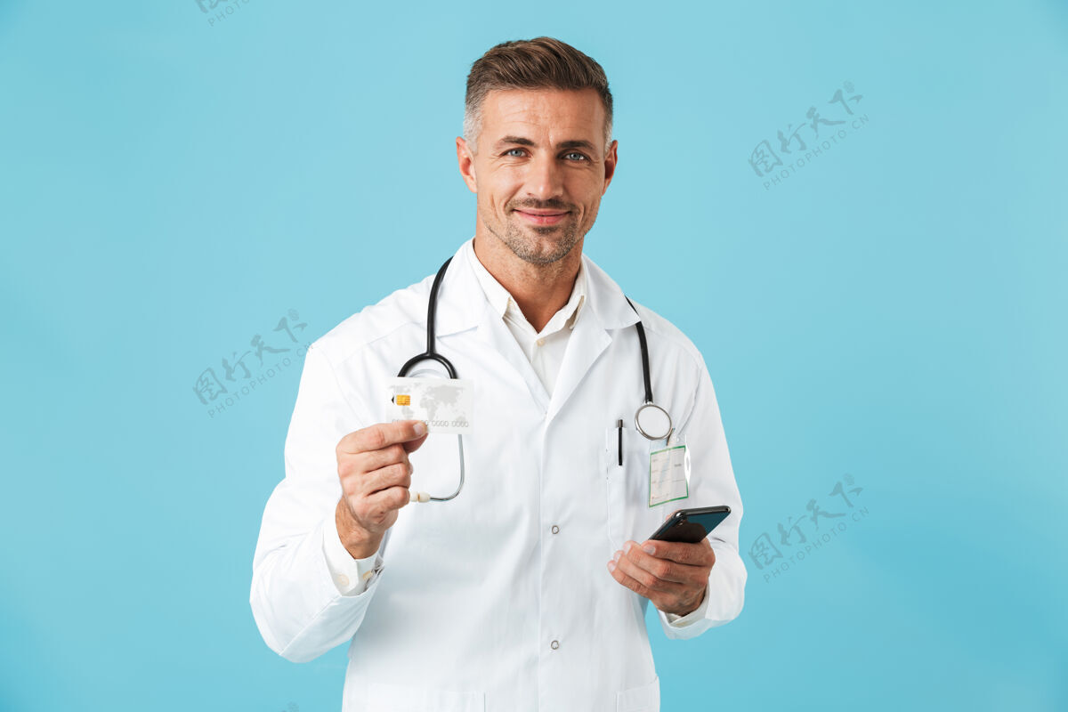 东西照片中的欧洲医生身穿白大褂 手持听诊器 孤立地站在蓝色的墙上男人成熟电话