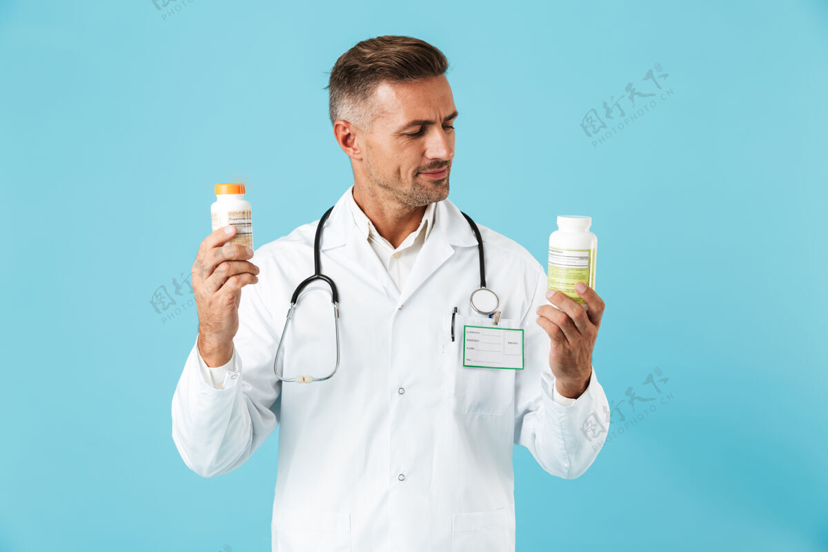 心脏病专家快乐的医学专家穿着白大褂 拿着几罐药 孤零零地站在蓝色的墙上中年人听诊器帅哥