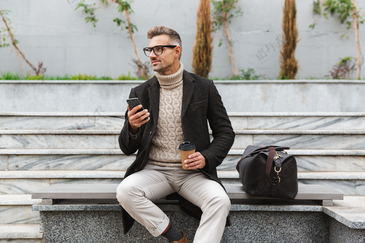 手机帅哥穿着夹克拿着手机 坐在户外喝外卖咖啡电话白种人男人
