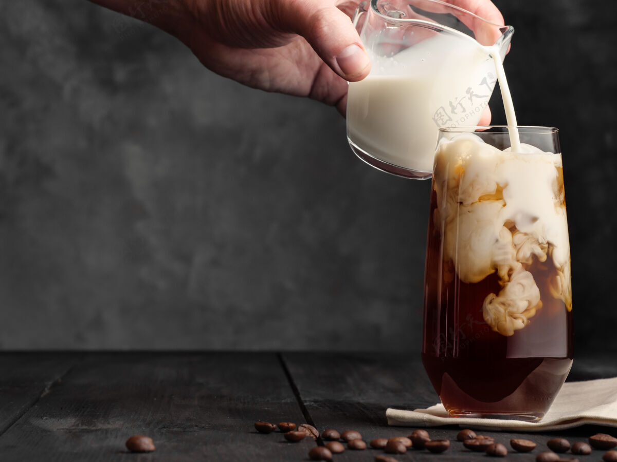 牛奶牛奶被倒入一个装有冰和咖啡的高球杯里 放在一张灰色的木桌上一壶咖啡加牛奶和冰饮料冷的咖啡
