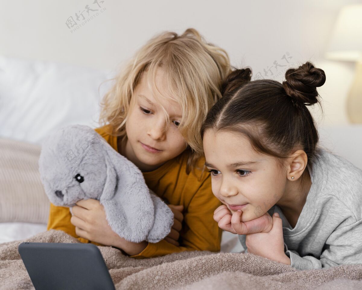 小玩意兄弟姐妹在床上看手机视频设备女孩室内