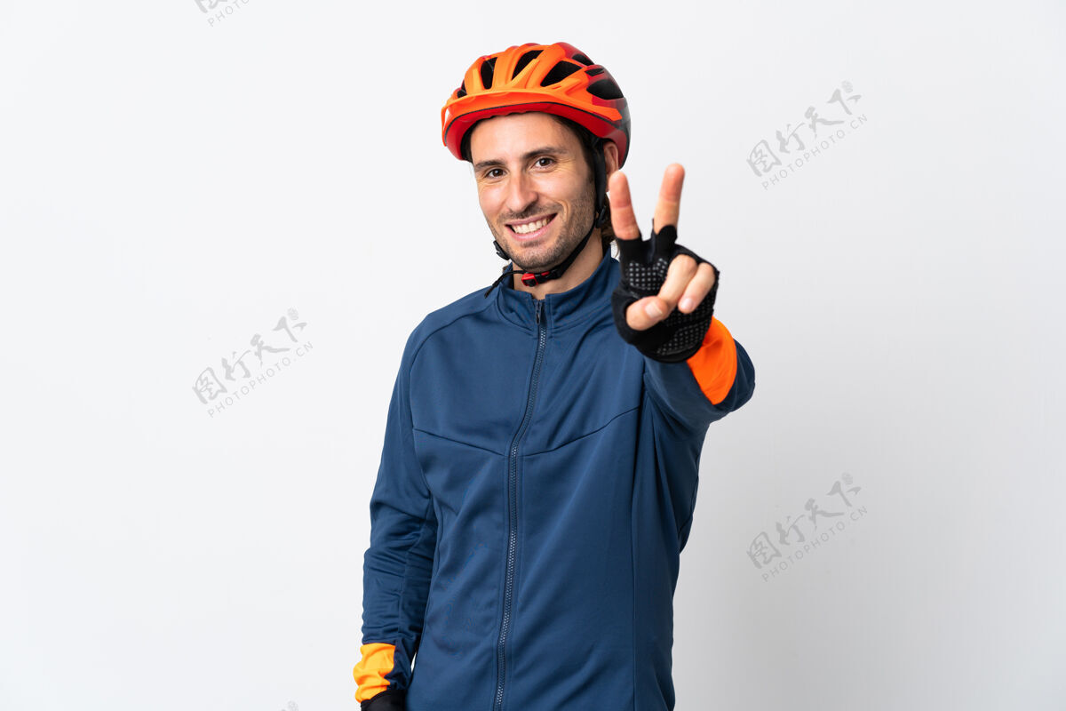 男性被隔离在白墙上的骑自行车的年轻人微笑着展示胜利的标志人运动装手