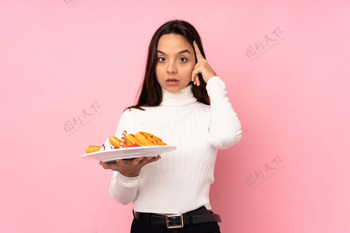 糕点年轻的黑发女人拿着华夫饼在孤立的粉红色墙上想着一个主意表达表达华夫饼