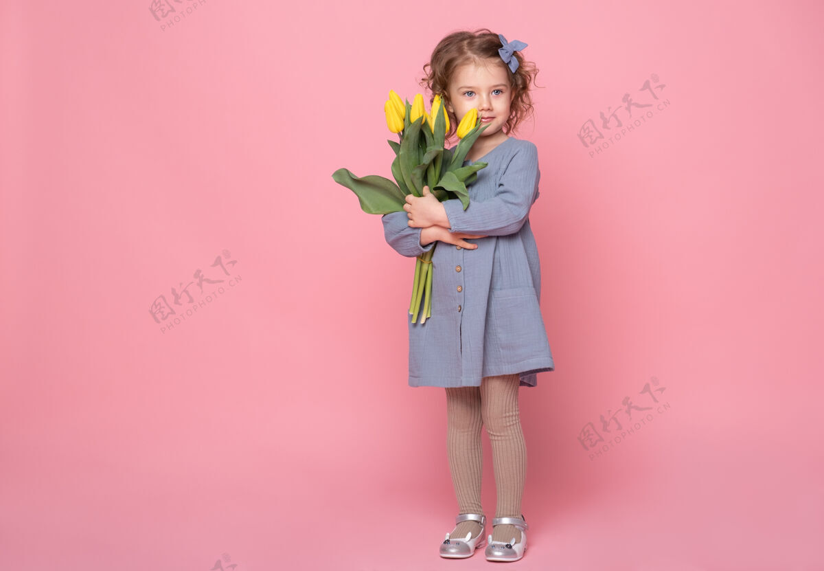 美丽美丽的金发小女孩穿着蓝色的裙子 粉色的裙子上有一束黄色的郁金香花束郁金香庆祝