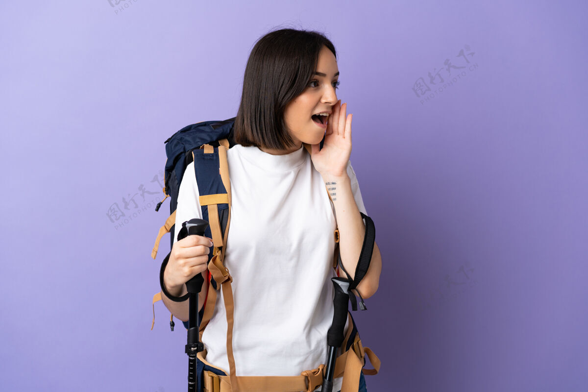 小径年轻的高加索妇女背着背包和登山竿 孤零零地站在蓝色的墙上 张大嘴巴一边喊着设备休闲背包