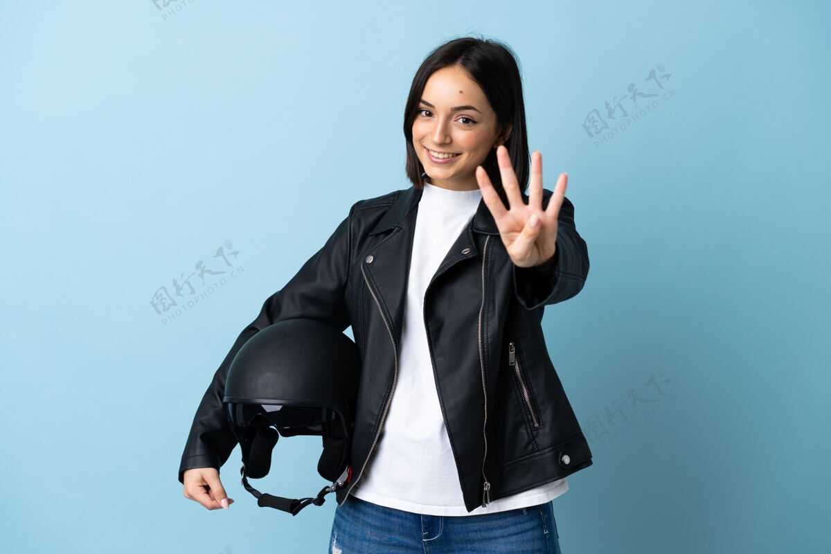 夹克一个戴着摩托车头盔的女人被隔离在蓝色的墙上 高兴地用手指数着四个司机计数数字