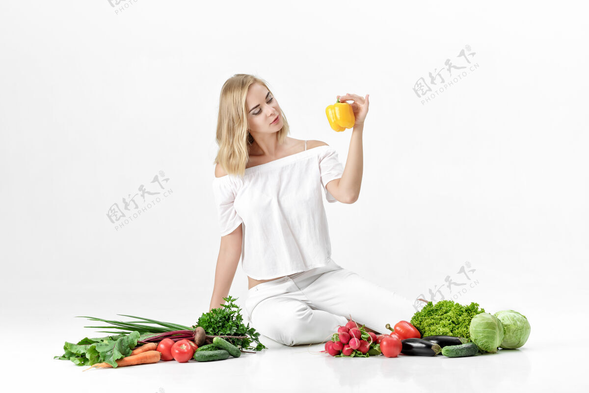漂亮漂亮的金发女人 穿着白衣服 白色的桌子上放着很多新鲜蔬菜背景女孩拿着甜椒有机蔬菜胡萝卜