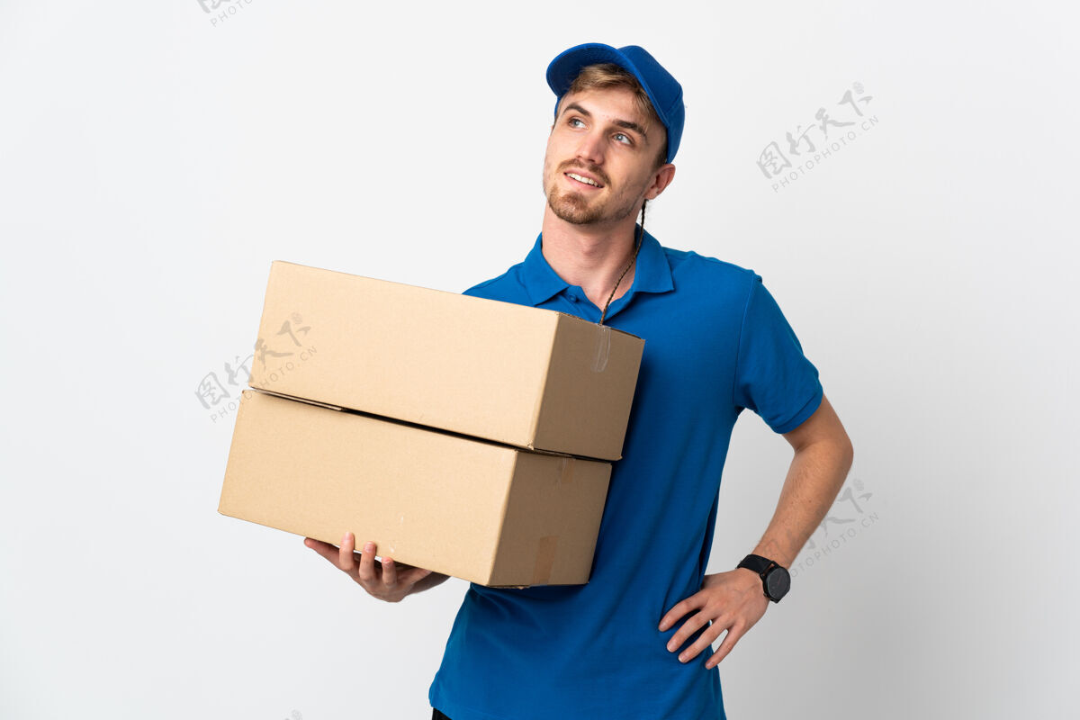 送货在白色背景下 一个年轻的金发男人摆出双臂放在臀部微笑的姿势送货年轻人商店