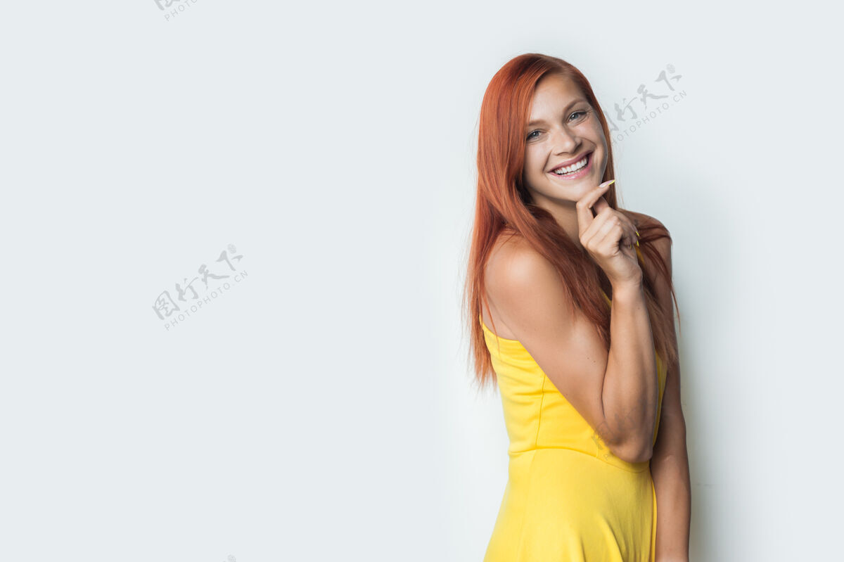 站立一个穿着红裙子和黄裙子的可爱女人正站在一堵白墙上抚摸着她的下巴女人空白红发