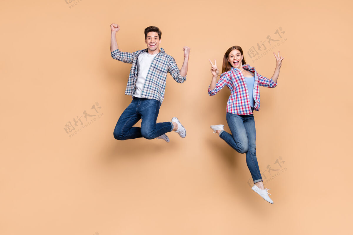 爱情两个人疯狂的女人家伙跳高显示v符号庆祝成功胜利穿休闲格子牛仔裤衣服孤立米色背景的全长照片乐趣运动兴奋