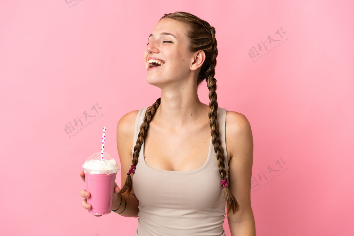 表情一个拿着草莓奶昔的年轻女人站在粉色背景上笑着年轻大笑女性