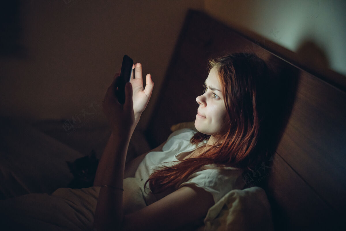 在线晚上 女人从床上爬起来 手里拿着一部电话休息虚拟房间女性通讯放松