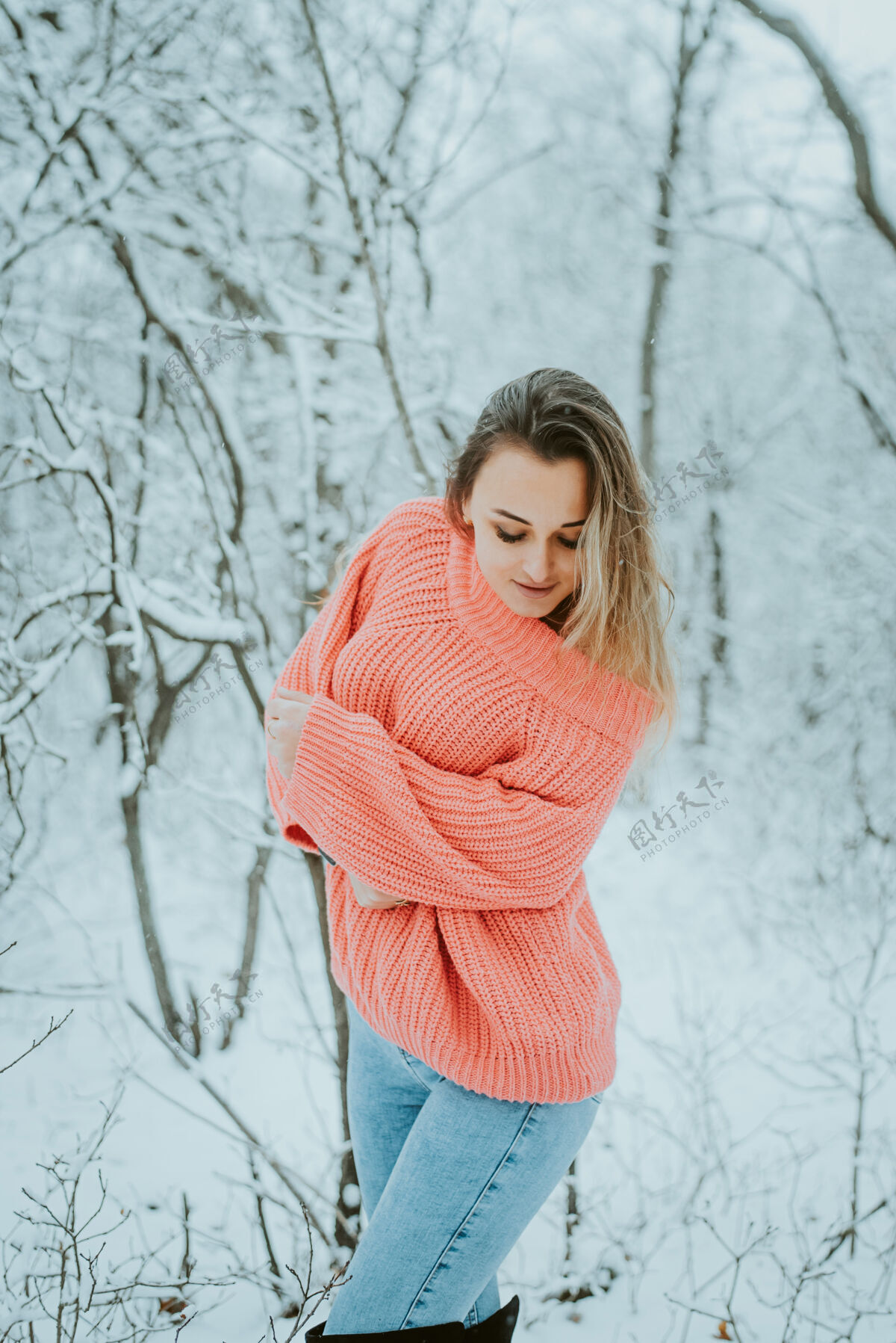 年轻一个穿着粉色宽松毛衣和牛仔裤的漂亮女孩在寒冷的雪域森林里享受性感新鲜