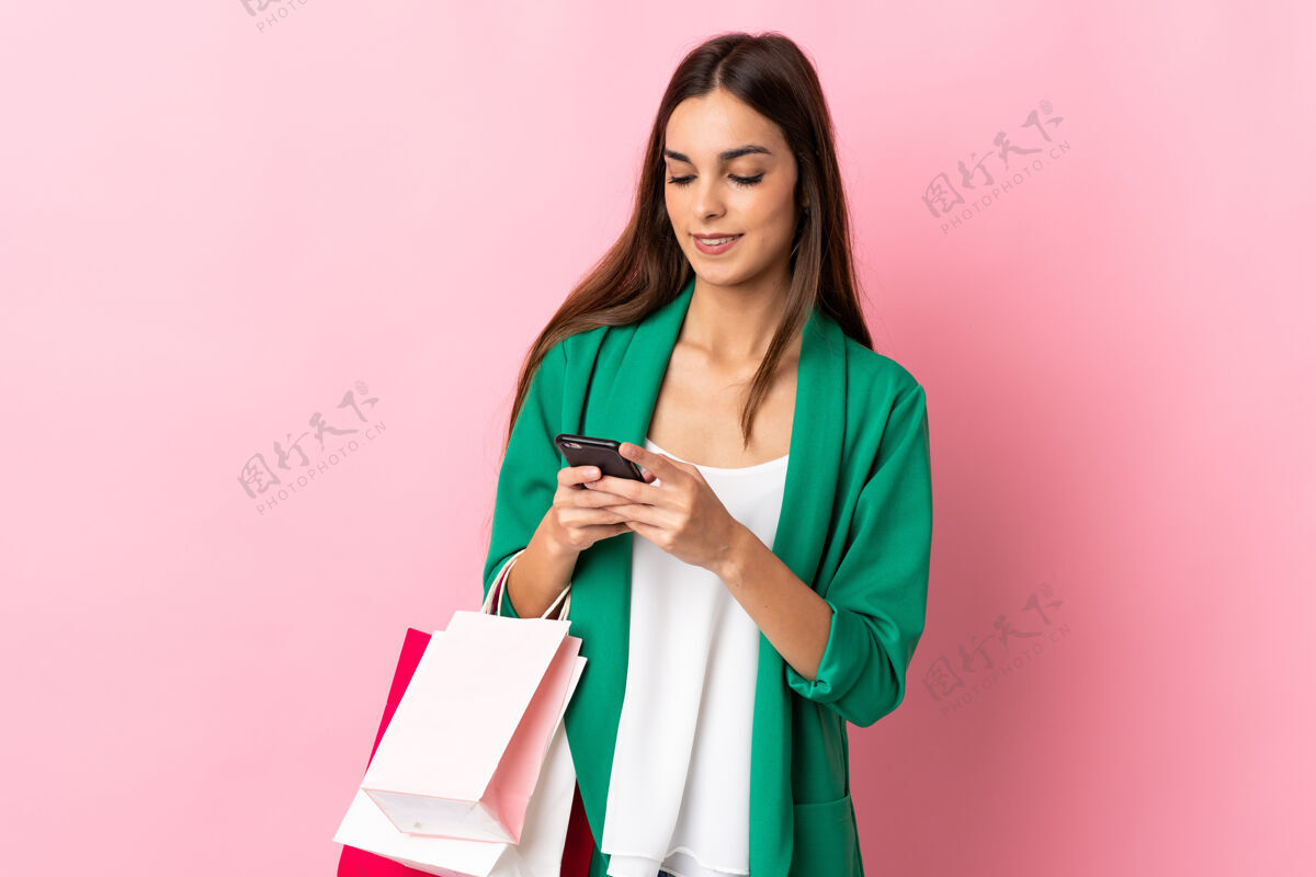 容器一位年轻的白人女性 手拿购物袋 拿着手机给一位朋友写信息 背景是粉红色的电话女人购买