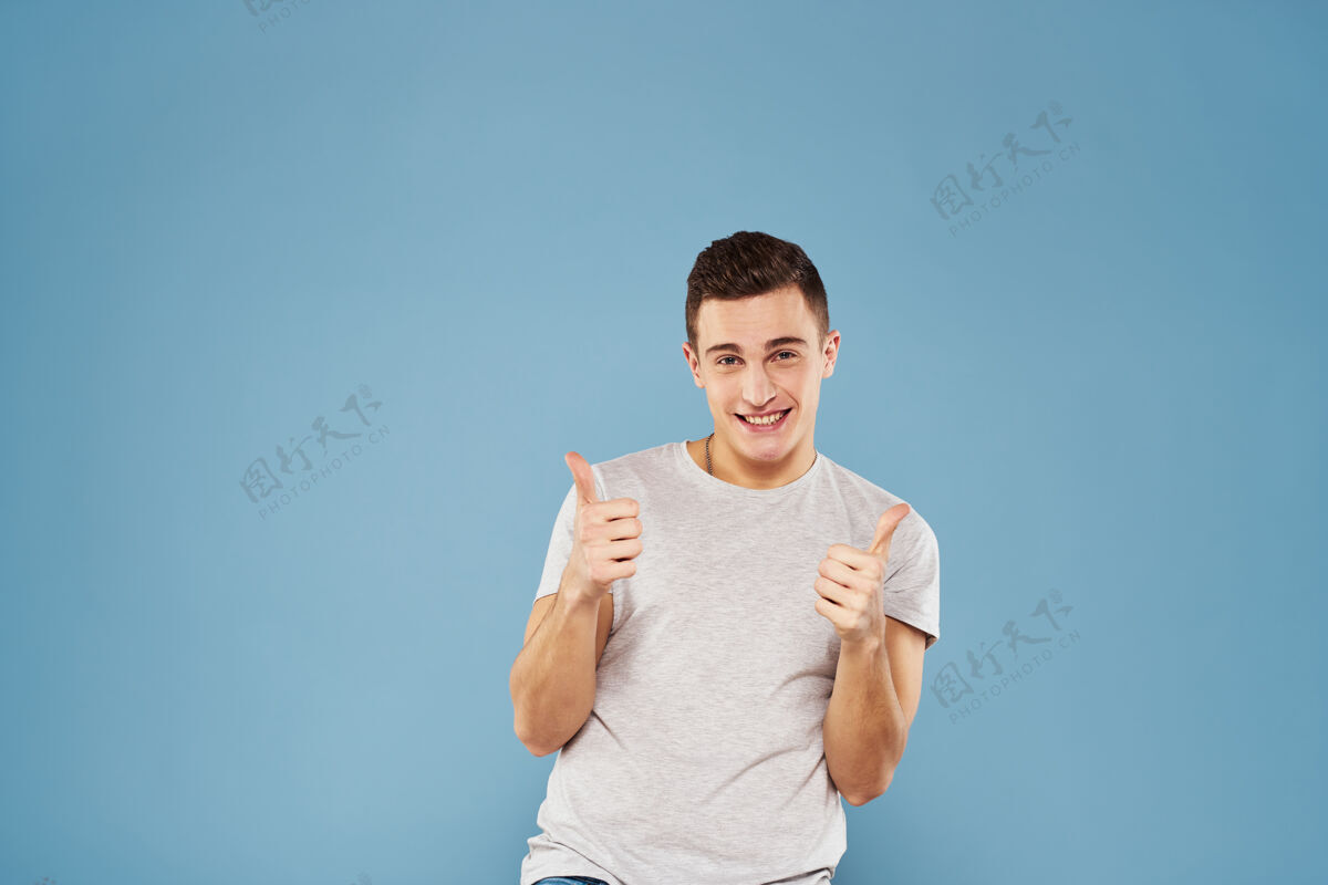 手指一个穿着白色t恤的快乐男人用手在蓝色的墙上做手势现代表情胡须