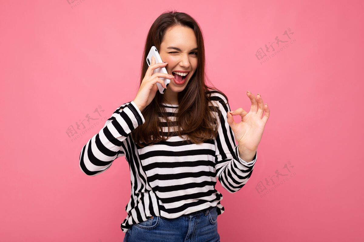 手机在电话里 一个穿着条纹毛衣的年轻女子正在眨眼 背景上有一块空白 看起来很好 看着相机嗨通信年轻